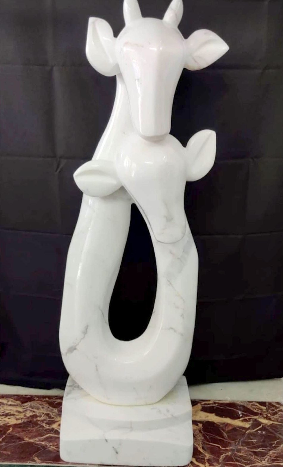 Scultura contemporanea in marmo bianco con due teste di cervo stilizzate su una forma ad anello, in un laboratorio partner