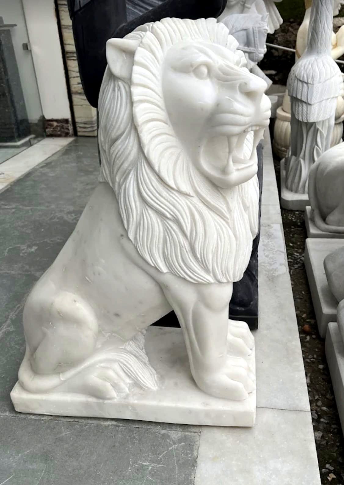 Leone seduto scolpito a mano in marmo bianco con criniera dettagliata, in un laboratorio di scultura partner