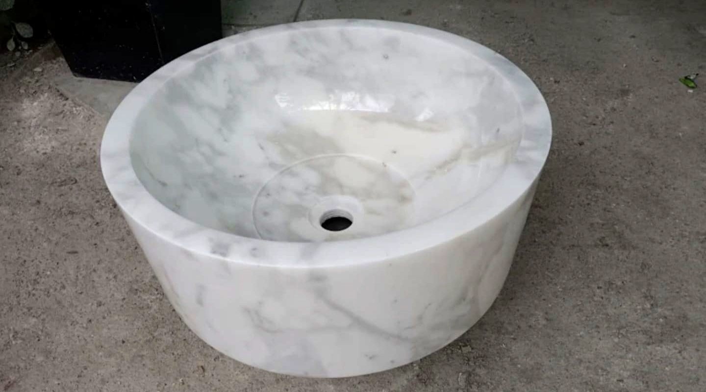 Lavabo da appoggio rotondo in marmo bianco con venature grigie e foro di scarico, in un laboratorio partner