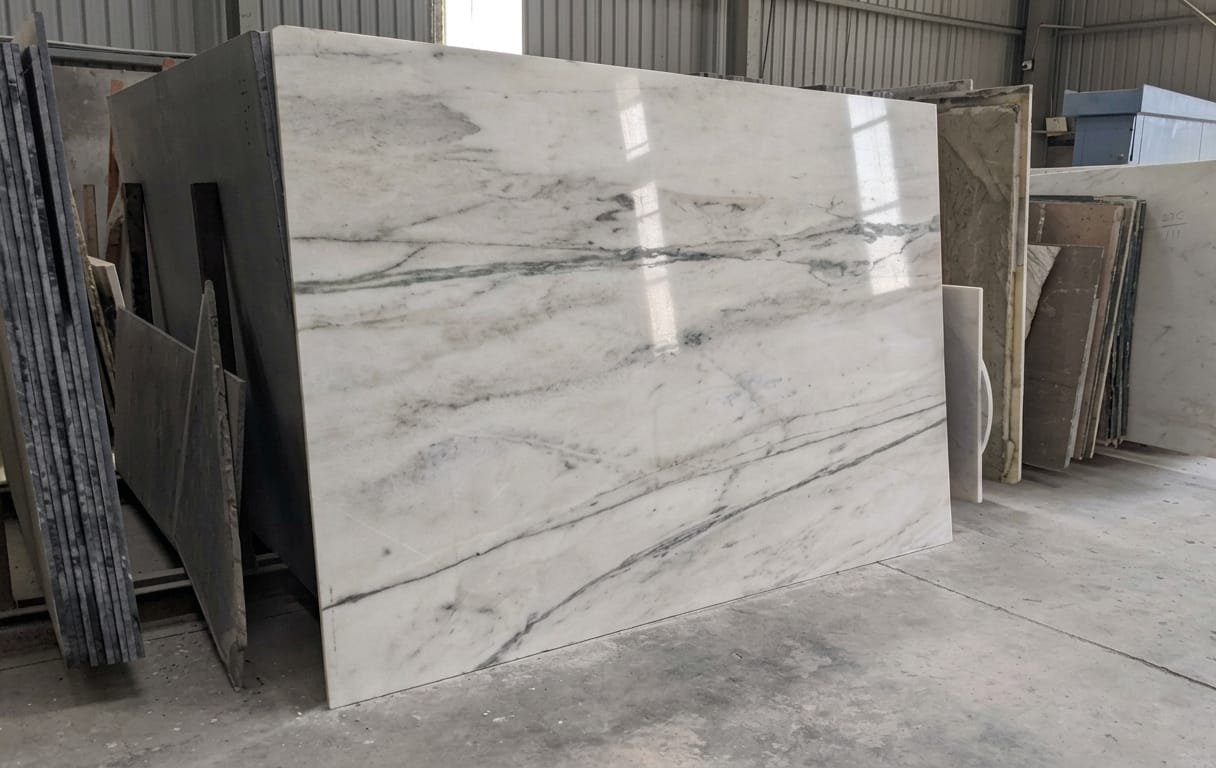 Polished white Indian marble slab with grey-green veining, standing in a partner processing unit in Rajasthan